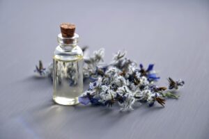 Glass bottle of essential oils with flowers next to it.