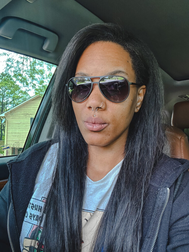 girl with long black hair sitting in her car wearing Sojos black aviator sunglasses