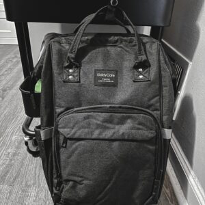 Dark Grey Backpack style Diaper bag in front of a 3-tier rolling cart